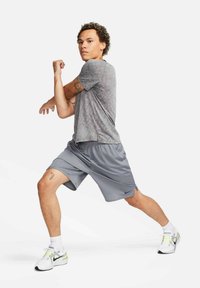 Šedé atletické tričko a šedé šortky s logom Nike. Model v pohybe, ktorý predvádza textúru látky a pružnosť športového oblečenia.
