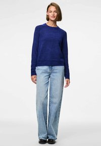 Sīki zila adīta džempera ar garām piedurknēm, apaļu kakla izgriezumu un strukturētu apdari komplektā ar plaša piegriezuma gaišo zilo džinsu un melnām kurpēm.