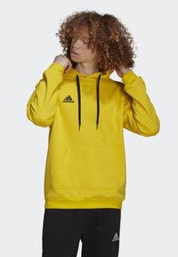 Gul sweatshirt med hætte, justerbare snore, frontlomme, sorte detaljer og Adidas-logo på brystet. Glat stof, afslappet pasform.