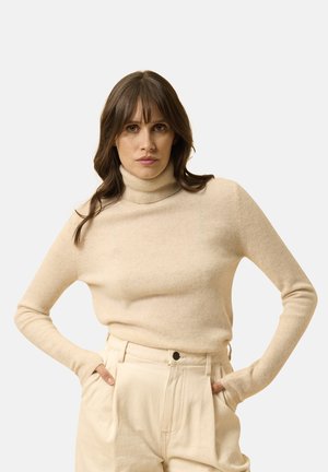 Beige coltrui gemaakt van zachte stof, voorzien van lange mouwen en een slim fit, gecombineerd met lichtgekleurde, relaxte broeken.