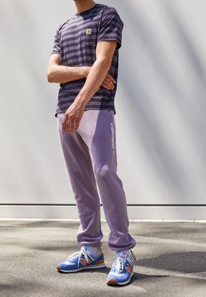 Striped navy and gray t-shirt with pocket, purple sweatpants, blue and tan sneakers. Outfit combines soft materials with distinct color contrasts.