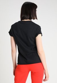 Černé tričko s krátkým rukávem a ohrnutými rukávy, kulatým výstřihem a pohodlným střihem, doplněné jasně červenými kalhotami.