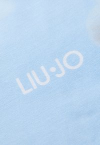 Tessuto azzurro chiaro con il testo bianco "LIU·JO" in una stampa prominente. La texture è liscia e leggermente lucida.