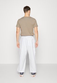 Brun t-shirt med kort ärm som är kombinerad med vita cargo-byxor. Byxorna har fickor och en avslappnad passform, stylerad med avslappnade sneakers.