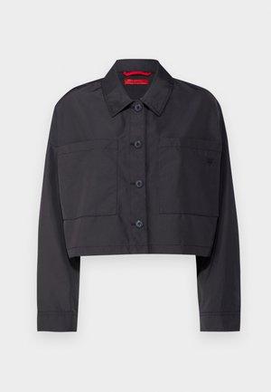 Zkrácená černá bunda s límečkem, zapínání na přední knoflíky, dvě náprsní kapsy a decentní logo detail na levé straně.