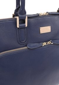 Sac à main en cuir marine avec quincaillerie dorée, dotée d'une fermeture à glissière, de poignées doubles et d'une poche zippée externe. Texture lisse et design structuré.