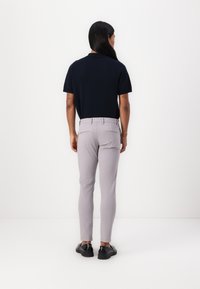 Marinefarbendes Poloshirt mit kurzen Ärmeln, kombiniert mit hellgrauen, schmal geschnittenen Hosen, die eine glatte Textur und standardmäßige Gesäßtaschen aufweisen. Schwarze Schuhe runden den Look ab.