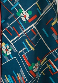 Tissu en satin mettant en valeur un fond bleu avec des motifs géométriques colorés et des fleurs blanches. Accentué de contours rouges et de formes variées.