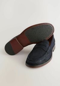 Mocasines de ante azul marino con punta redondeada suave, detalles de costura y una suela de goma marrón con agarre texturizado.