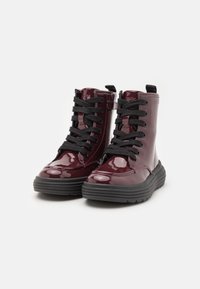 Burgundy patent leather ankle boots with black laces, rounded toe, and a thick rubber sole. Features a side zipper and a pull tab.