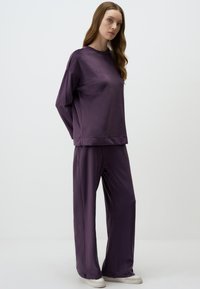 Ensemble lounge violet en tissu doux, comprenant un haut à manches longues avec col rond et un pantalon large, complété par des baskets blanches.
