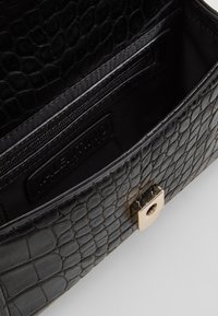 Interno della borsa in pelle sintetica effetto coccodrillo nero con tasca con zip e hardware dorato; presenta una superficie texture e stampata e una fodera liscia.