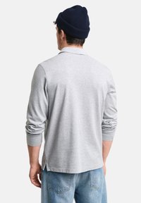Un polo gris à manches longues avec une texture douce et un col côtelé, associé à un jean en denim bleu clair. Un bonnet bleu marine est porté.