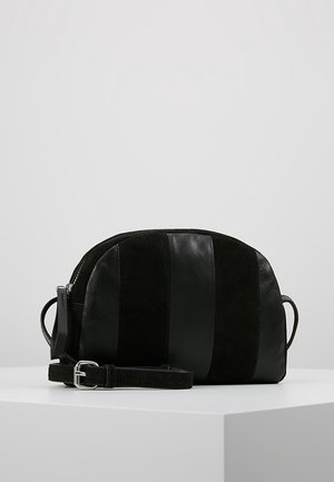 Sort crossbody taske med brede lodrette ruskind- og læderstriber, justerbar rem og lynlåslukning, vist på en hvid overflade.