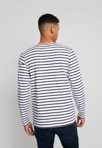 Camicia a maniche lunghe di colore bianco con strisce orizzontali nere. Presenta un collo a giro e una vestibilità comoda. Realizzata in un tessuto morbido e leggero.