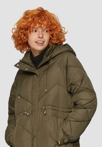 Gequilted olijfgroene pufferjack met een capuchon, voorzien van zilveren hardware en verstelbare trekkoorden, een getextureerde stof en zijzakken.