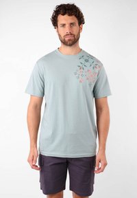 T-shirt en coton bleu clair avec des impressions florales orange et bleu-vert sur l'épaule gauche ; col rond ; manches courtes ; coupe décontractée.