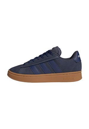 Zapatilla Adidas azul marino con tres franjas, suela de goma marrón, cierre de cordones y logo de Adidas en el talón y en el lateral de la suela.