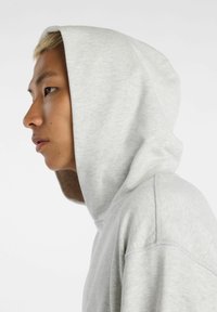 Light gray hooded sweatshirt with a soft texture, featuring a prominent hood and stitching detail, displayed from a side profile view.