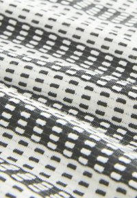 Tessuto a maglia con un motivo ripetitivo di piccoli quadrati neri su uno sfondo bianco, con una finitura morbida e strutturata.