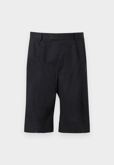 Shorts noirs sur mesure longueur genou avec passants pour ceinture et plis à l'avant, posés à plat sur un fond gris clair.
