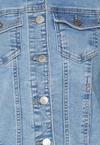 Chaqueta de mezclilla de color azul claro con cierre de botones, dos bolsillos en el pecho y un cuello clásico. La tela tiene una apariencia texturada y ligeramente desgastada.