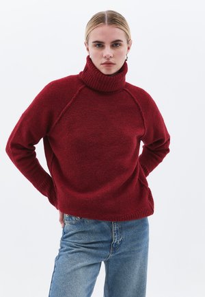 Rød, chunky striktrøje med en høj, ribbet turtleneck, raglanærmer og en afslappet pasform. Sæt sammen med lyseblå jeans.