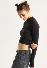 Black crop top with long sleeves, made of a smooth fabric, featuring a high neckline and subtle branding on the front.