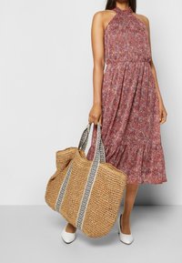Blommig klänning i nyanser av rött och rosa, med halterneck och volangkant, kombinerad med en stor stråväska med mönstrade remmar.
