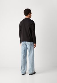 Musthave musta pikkade varrukatega särk, ümara kaelusega, sobitatud helesiniste laia säärega teksade ja mustade kingadega. Sile tekstuur, minimalistlik disain.