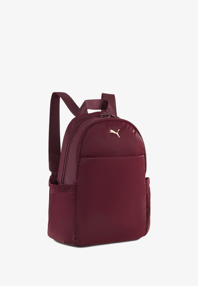 Zaino marrone con una texture liscia e imbottita, dotato di spallacci regolabili e di un logo dorato. Include una tasca frontale e scomparti laterali in rete.