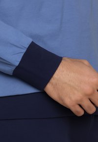 Blue and navy long-sleeve shirt featuring contrasting ribbed cuffs and smooth texture, showcasing a relaxed fit and layered look.