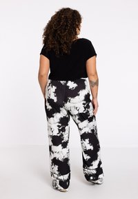 Zwarte top met korte mouwen gecombineerd met wijde broek met een zwart-wit abstract patroon. Glad materiaal met een elastische tailleband.