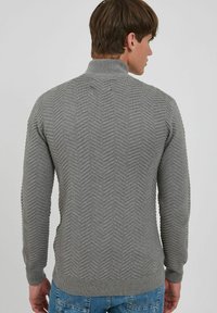 Grå striktrøje med høj krave, som har et struktureret zigzag-mønster, ribbede manchetter og talje. Bæres med blå jeans.