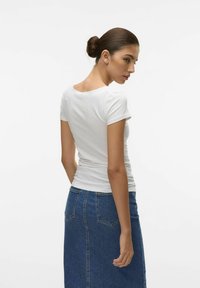 Camicia bianca a maniche corte con scollatura rotonda, abbinata a una gonna di jeans blu a vita alta con due tasche posteriori e taglio dritto.