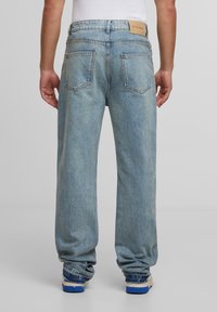 Jeans din denim de un albastru deschis, cu o croială lejeră, având o etichetă din piele la talie și două buzunare spate cu detalii de cusătură vizibile.