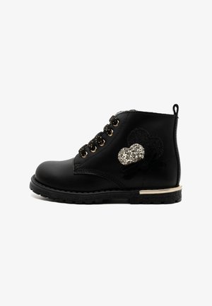 Black ankle boot, leather material, gold eyelets, flat sole, adorned with black and silver glitter hearts, stitched detailing, and a looped back tab.