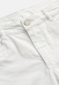 Hvid denimjeans linning med lukning i metalknap, bæltestropper og synlige syningsdetaljer.