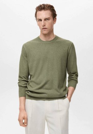 Olivgrüner Strickpullover mit langen Ärmeln, runder Halslinie, strukturiertem Gewebe und lockerer Passform; kombiniert mit hellen Hosen.
