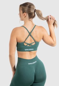 Sujeción verde con tirantes entrecruzados, hecha de material elástico. Presenta el logo "SMILODOX" en la banda y leggings de cintura alta a juego.