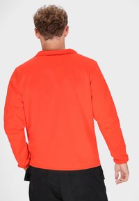 Langsleeve shirt in feloranje stof met een gladde textuur. Heeft een klassieke kraag en een eenvoudige achterkant. Gecombineerd met donkere pantalon.
