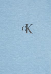 Světle modré bavlněné tričko s černým logem "cK" na přední straně. Hladká textura s jednoduchým a čistým designem.