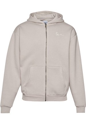 Svetlošedá bunda na zips vyrobená z mäkkej tkaniny, s prednou vreckom, rebrovanými manžetami a malým bielym logom na hrudi.
