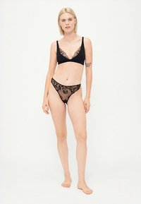 Black lace bralette with V-neck and sheer black lace thong featuring floral patterns. Soft texture, minimalist design. No hardware visible.