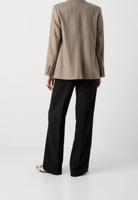 Hnědý blazer s jemným pruhováním a přiléhavým střihem, dlouhými rukávy, knoflíkovými manžetami, kombinovaný s černými kalhotami a světle zbarvenou obuví.