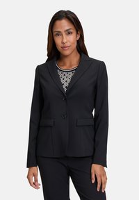Černá blazer s přiléhavým střihem, se dvěma knoflíky a klopovými límci. Obsahuje dvě přední kapsy a vzorovaný top pod ním.