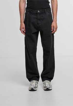 Black denim cargo pants with a relaxed fit, featuring side pockets, a zip detail, and contrast stitching. Paired with gray sneakers.