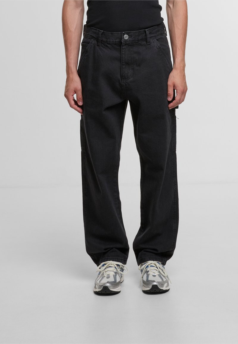 Pantalones cargo de mezclilla negra con un ajuste relajado, que cuentan con bolsillos laterales, un detalle de cremallera y costuras en contraste. Combinados con zapatillas grises.