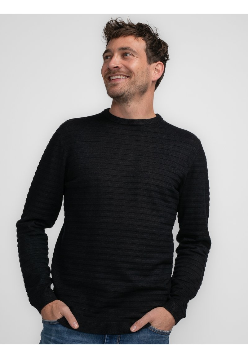 Maglione nero a maglia con coste orizzontali, collo a giro, e maniche lunghe, caratterizzato da una consistenza morbida e un orlo aderente. Indossato sopra dei jeans blu.