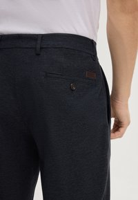 Navyblauwe broek van een gestructureerde stof, met een achterzak met een knoop en een leren logo-label.